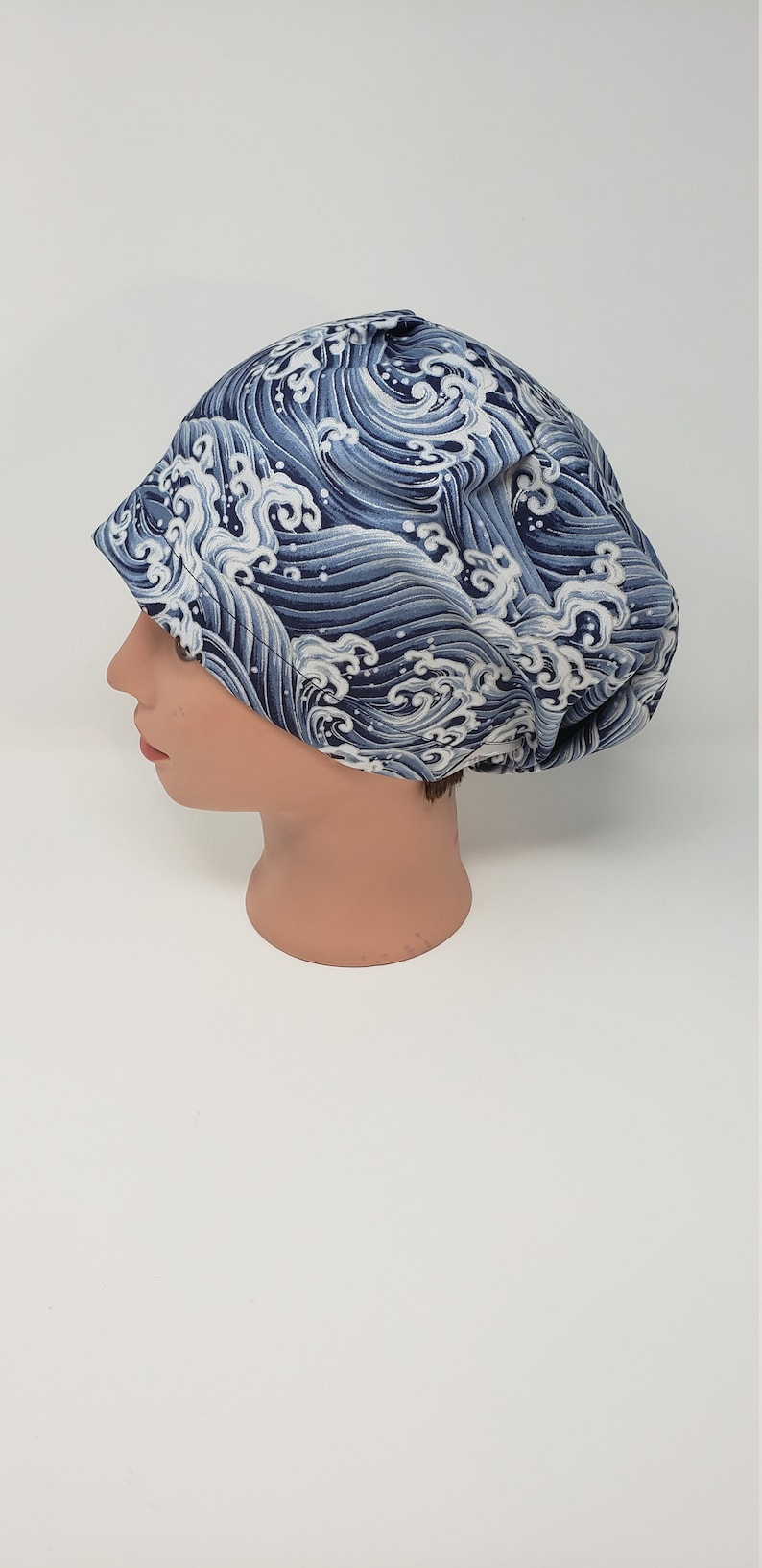May include: A blue and white patterned scrub cap. The cap features a repeating design of stylized ocean waves. The cap is made of a soft fabric and is designed to cover the hair.