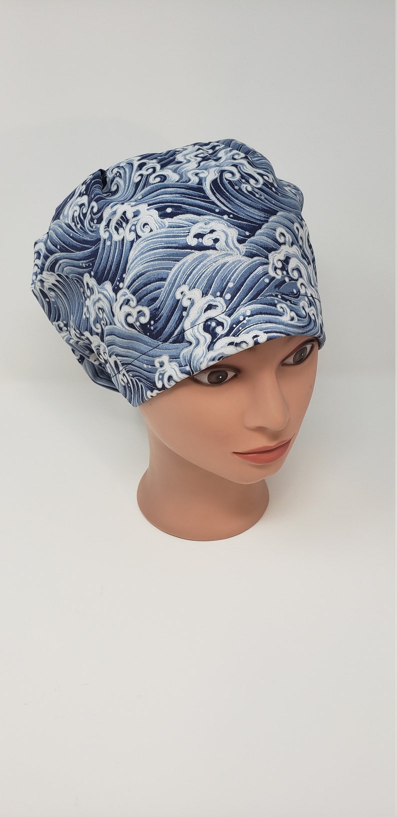 May include: A blue and white patterned scrub cap featuring a wave design. The cap is made of fabric and is designed to cover the head. The wave pattern is in shades of blue and white.