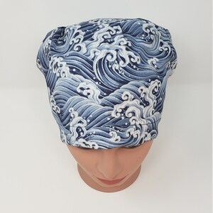 May include: A blue and white wave-patterned surgical scrub cap. The cap is made of fabric and is designed to cover the head. The wave pattern is a repeating design in shades of blue and white.