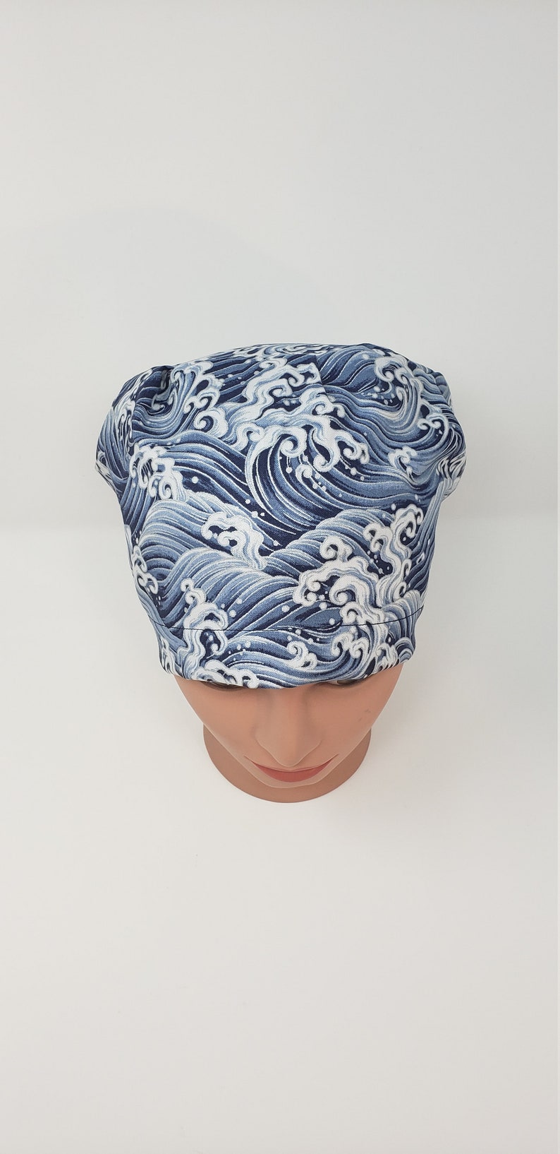 May include: A blue and white wave-patterned surgical scrub cap. The cap is made of fabric and is designed to cover the head. The wave pattern is a repeating design in shades of blue and white.