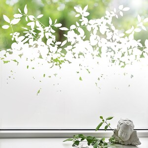 Könnte beinhalten: Weiße, gefrostete Fensterfolie mit einer Silhouette von Blattästen und Blättern. Die Folie ist auf ein Fenster mit weißem Rahmen angebracht. Auf der Fensterbank stehen eine kleine grüne Pflanze und eine weiße Cherubstatue.