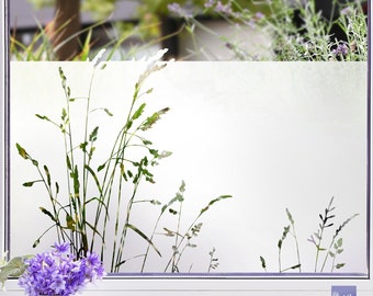 May include: A frosted window film with a silhouette of tall grass. The film is applied to a window with a white frame. The window is in a room with a vase of purple flowers on a white surface.