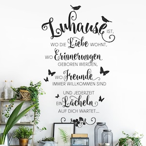 Op de afbeelding: Een witte muur met zwart script met de tekst: "Luhause ist, wo die Liebe wohnt, wo Erinnerungen geboren werden, wo Freunde immer willkommen sind, und jederzeit ein Lächeln auf dich wartet..." Decoratieve vlinders en vogels zijn ook inbegrepen.