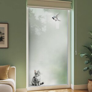 Könnte beinhalten: Ein Fenster mit einem Milchglasdesign, das eine Katze zeigt, die nach oben zu einem fliegenden Vogel blickt. Die Katze ist grau und weiß, und der Vogel ist schwarz und weiß. Das Fenster ist weiß umrahmt und vor einer grünen Wand platziert.