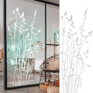 Op de afbeelding: Witte, gematteerde glasfolie voor ramen met een ontwerp van hoge grassilhouetten. De folie is aangebracht op een glazen deur in een kamer met een stoel en een houten tafel.
