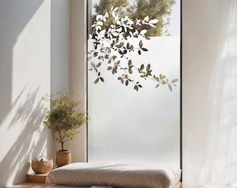 May include: A white frosted window with a silhouette of a leafy branch design. A bed with a white linen duvet and a brown throw blanket is in the foreground.