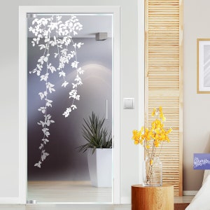 Könnte beinhalten: Eine Milchglastür mit einem weißen, geätzten Design aus Blattranken. Die Tür ist weiß umrahmt und hat einen silbernen Griff. Die Tür ist geöffnet und gibt den Blick auf einen Raum mit einer weißen Topfpflanze und einer hellgrauen Wand frei.