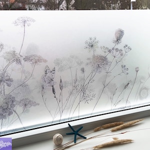 Könnte beinhalten: Eine Milchglasfolie mit einem zarten Design aus schwarzen und weißen Wildblumen und einem Schmetterling. Die Folie ist auf ein Fenster mit weißem Rahmen angebracht.