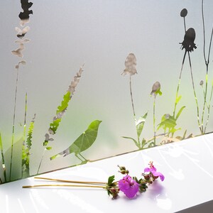 May include: A frosted glass window pane with a silhouette design of various plants and a bird. A bouquet of pink flowers sits on a white surface below the window.
