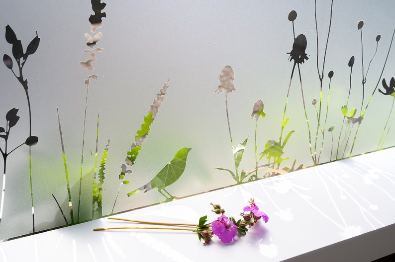 May include: A frosted glass window pane with a silhouette design of various plants and a bird. A bouquet of pink flowers sits on a white surface below the window.