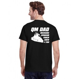 May include: Black t-shirt featuring a white race car graphic and the words "QM DAD, MECHANIC, SPONSOR, COACH, CREW, #1 FAN". The shirt has a crew neck design.