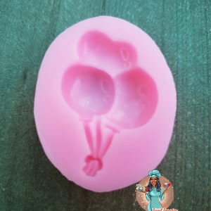 May include: Pink silicone mold for making three balloon shaped cake decorations. The mold is shaped like an oval and has three balloon shapes with strings.