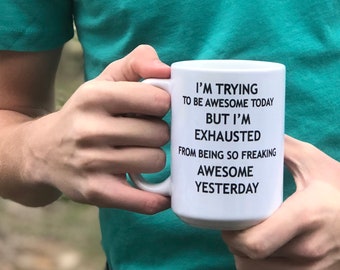 May include: White coffee mug with black text that reads "I'm trying to be awesome today but I'm exhausted from being so freaking awesome yesterday."