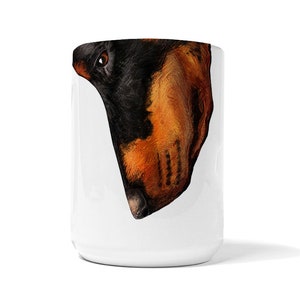 May include: White ceramic mug with a black and brown dog's head printed on it. The dog's head is tilted to the side and the dog's nose is visible.