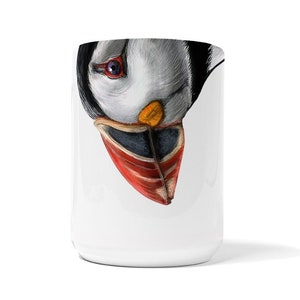 May include: White ceramic mug with a colorful illustration of a puffin's face looking down at the viewer. The puffin's beak is orange, red, and black.