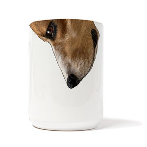 May include: White ceramic mug with a brown and white dog's face printed on it. The dog's face is upside down and the dog is looking at the viewer.