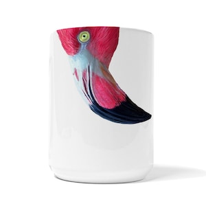 May include: A white ceramic mug with a pink flamingo head peeking over the rim. The flamingo's eye is visible, and its beak is black with a pink tip.