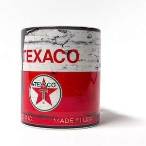 May include: A white ceramic mug with a vintage Texaco gas can design. The mug features a red, white, and green Texaco logo with a star and the letter "T". The text "Texaco" is printed in red on the mug. The mug is made in the USA.