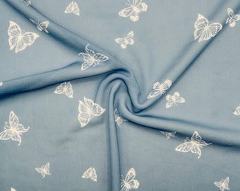 May include: A close-up of a blue fabric with a white butterfly pattern. The butterflies vary in size and are scattered across the material. The fabric is gathered in a swirl, showing the texture and folds of the material.