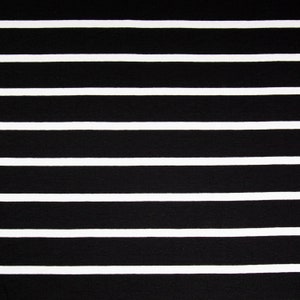 May include: Close-up of a fabric with a black and white striped pattern. The stripes are horizontal, with thick black bands alternating with thinner white bands. The fabric appears to be a textile, possibly for clothing or home decor.