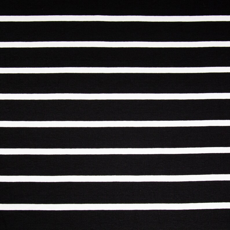 May include: Close-up of a fabric with a black and white striped pattern. The stripes are horizontal, with thick black bands alternating with thinner white bands. The fabric appears to be a textile, possibly for clothing or home decor.