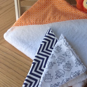 Pu&ograve; includere: Tre bavaglini per neonati bianchi con diversi motivi. Un bavaglino ha uno sfondo bianco con cerchi arancioni, un altro ha uno sfondo bianco con zig zag blu scuro e l'ultimo ha uno sfondo bianco con barche blu scuro.