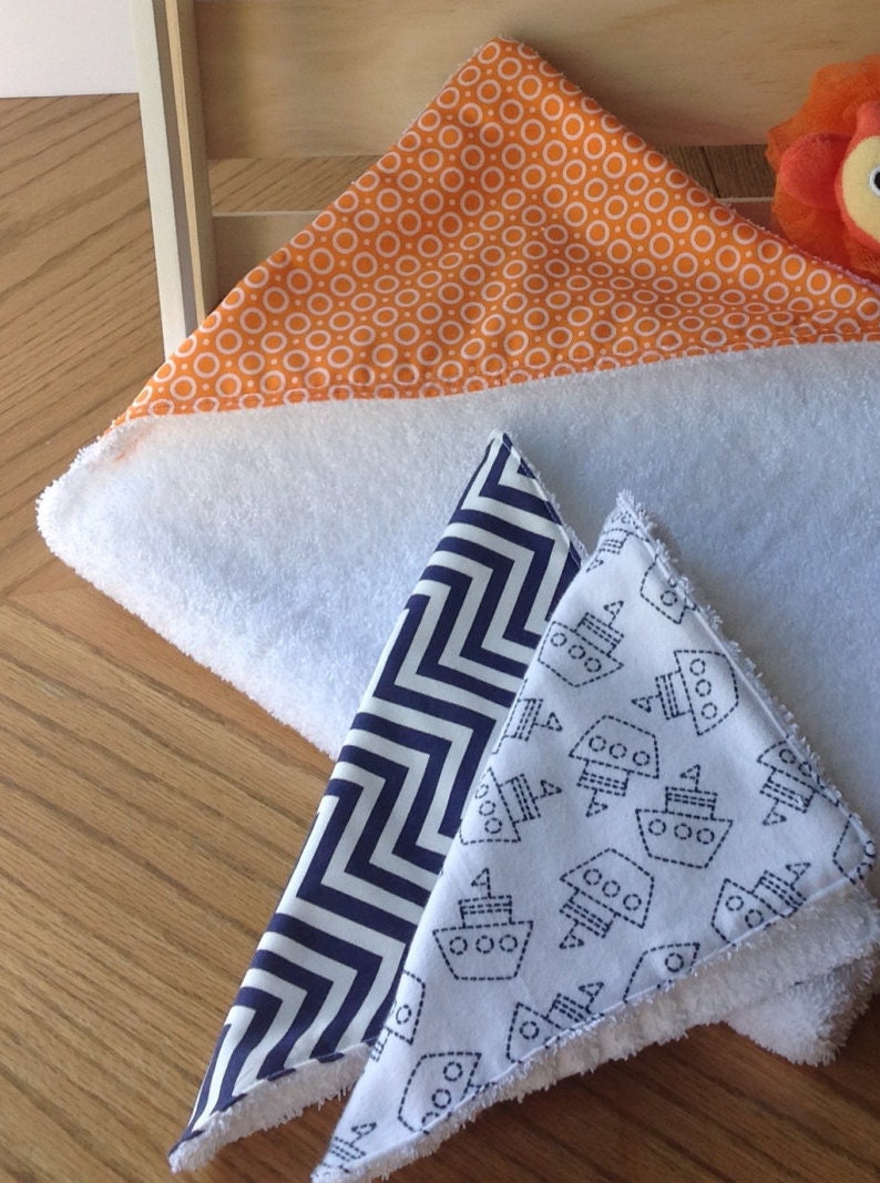 Pu&ograve; includere: Tre bavaglini per neonati bianchi con diversi motivi. Un bavaglino ha uno sfondo bianco con cerchi arancioni, un altro ha uno sfondo bianco con zig zag blu scuro e l'ultimo ha uno sfondo bianco con barche blu scuro.