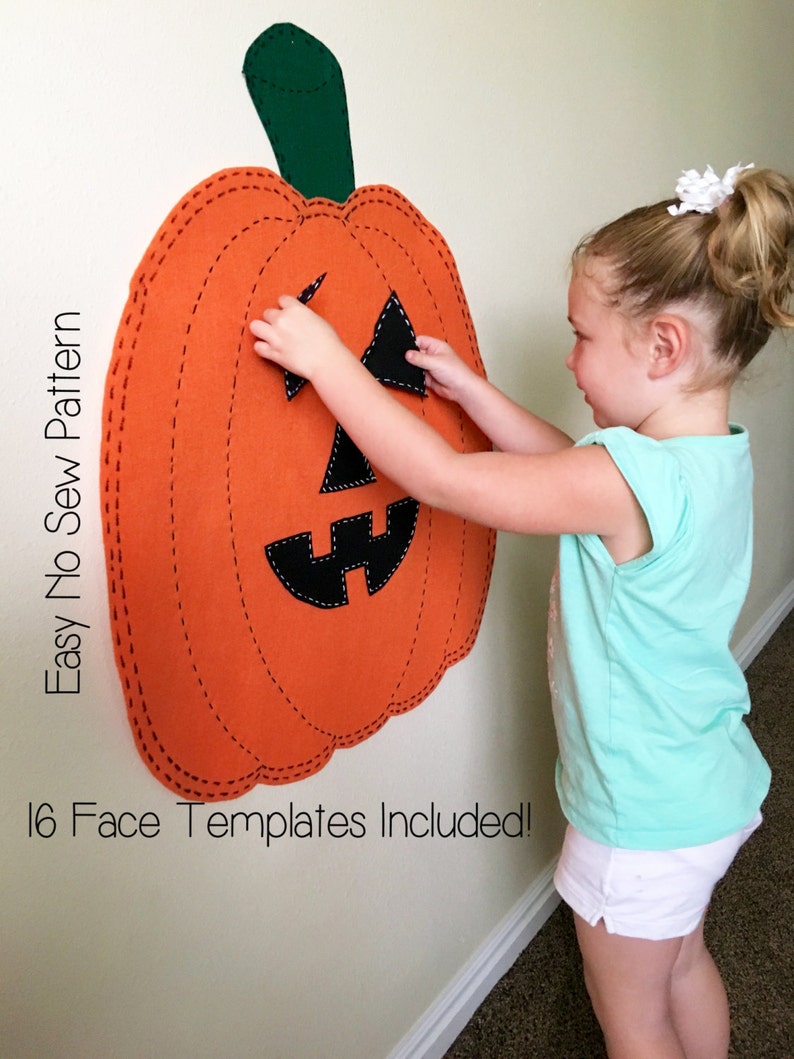 May include: A child places a black felt face piece on a large orange felt pumpkin with a green felt stem. The pumpkin is attached to a white wall. The text "Easy No Sew Pattern" is written vertically on the left side of the pumpkin. The text "16 Face Templates Included!" is written below the pumpkin.