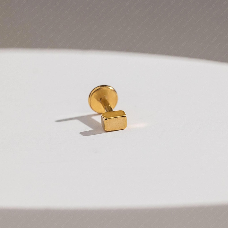 A small gold-colored metal object, possibly a pin or earring, is resting on a white surface.