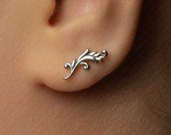 May include: A silver-toned ear climber earring featuring a delicate, curved botanical leaf design with multiple small, pointed segments. The piece follows the natural contour of the earlobe, showcasing a polished metallic finish and intricate scrollwork.