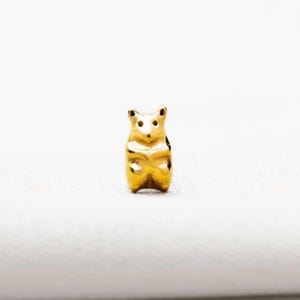 A small golden bear charm is sitting on a white surface.