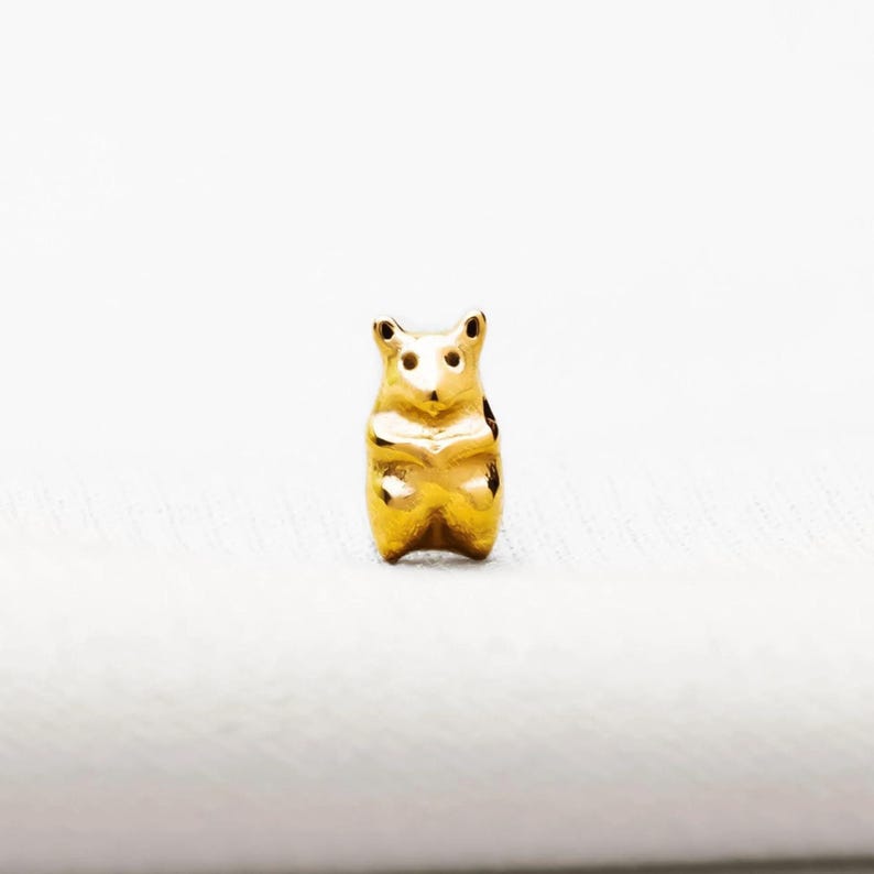 A small golden bear charm is sitting on a white surface.