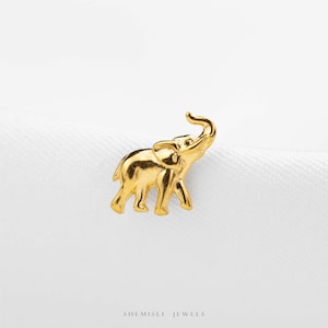 May include: A small, polished gold-tone stud earring shaped like a walking elephant with its trunk raised upward. The elephant figure features smooth, reflective surfaces and detailed ear and leg contours. The text SHEMISLI JEWELS is visible below.