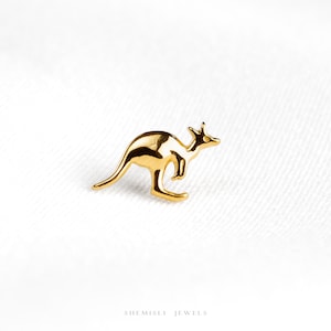 May include: A small, polished gold-toned stud earring shaped like a kangaroo in a standing profile position. The metal surface is smooth and reflective, capturing light to highlight the distinct silhouette of the animal's head, ears, and tail.