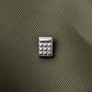 A close-up image of a small metal calculator pin resting on a textured fabric surface.