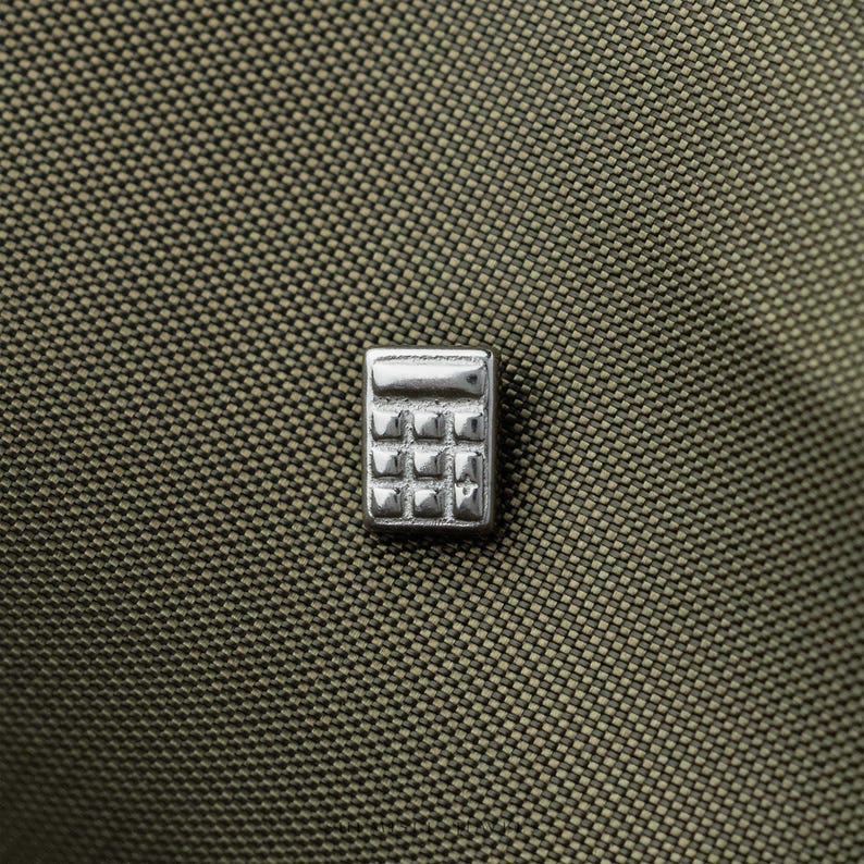 A close-up image of a small metal calculator pin resting on a textured fabric surface.