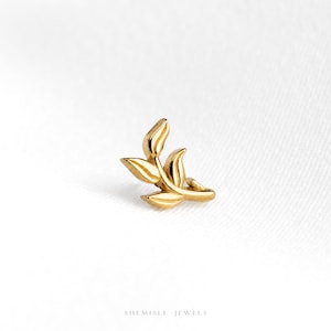 May include: A gold-toned stud earring shaped like a small leafy branch with three distinct leaves. The piece features a polished metallic finish and is positioned against a plain white background. The text SHEMISLI JEWELS is printed at the bottom.