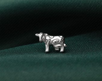 May include: A small, silver-toned metal stud earring shaped like a cow. The cow figure features a smooth, reflective surface with embossed circular spots across its body and head. The text "SILIMISLI JEWELS" is printed in small letters at the bottom.