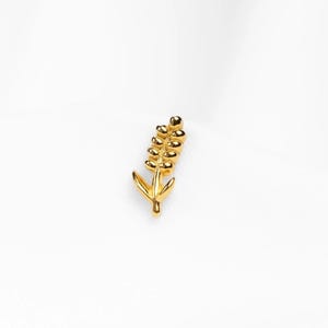 May include: A gold-colored, wheat-shaped pin. The pin features a detailed design of a wheat stalk with multiple grains and two leaves at the base. The pin is set against a white background.