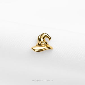 May include: A gold-colored witch hat charm with a buckle on the brim. The charm is set against a white background. The words "SHEMISLI JEWELS" are at the bottom of the image.