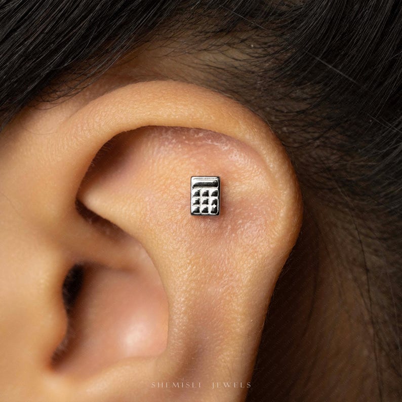 A small silver calculator-shaped earring is visible in the person's ear.