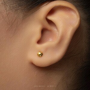 A close-up of a person's ear with a small gold-colored earring inserted.