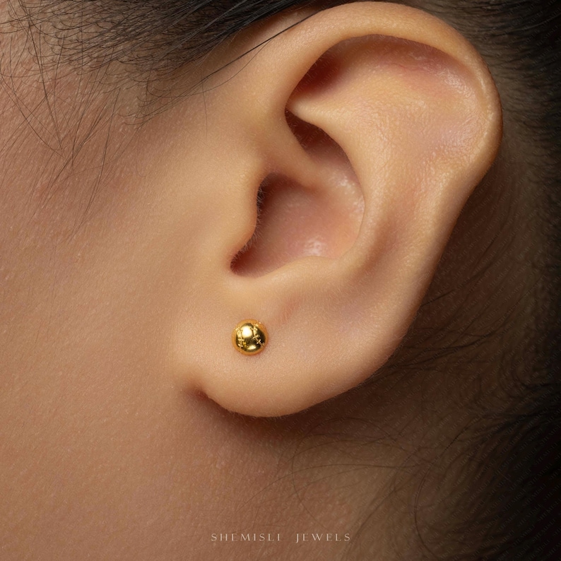 A close-up of a person's ear with a small gold-colored earring inserted.