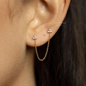 A close-up view of a person's ear adorned with a delicate gold chain earring featuring a small diamond-like stone.