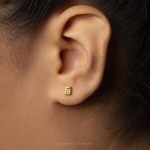 A close-up view of a person's ear with a small gold earring in the earlobe.