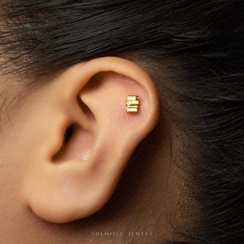 A close-up of a person's ear with a small gold earring in the earlobe.