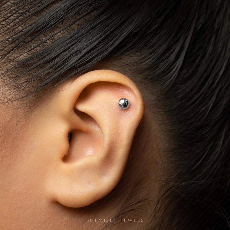 A close-up of a person's ear with a silver earring in the earlobe.