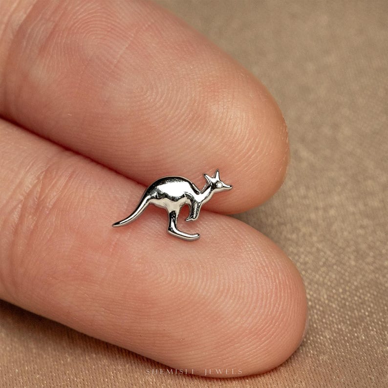 a small silver kangaroo brooch sitting on top of a person's finger