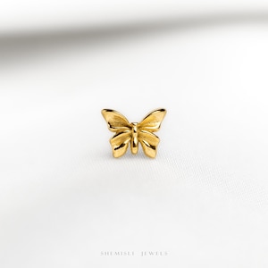 May include: A small gold-toned butterfly stud earring with a polished finish and symmetrical wings. The piece features a central body and detailed wing segments. Below the butterfly, the text SHEMISLI JEWELS is printed in a clean, sans-serif font.