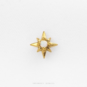 May include: A gold-toned star-shaped stud earring featuring a central round iridescent white opal stone. The metal star has four primary points and four smaller points between them. The text SHEMISLI JEWELS is printed at the bottom.